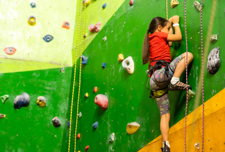 photo of a kid climbing with safety harness at indoor climbing wall.